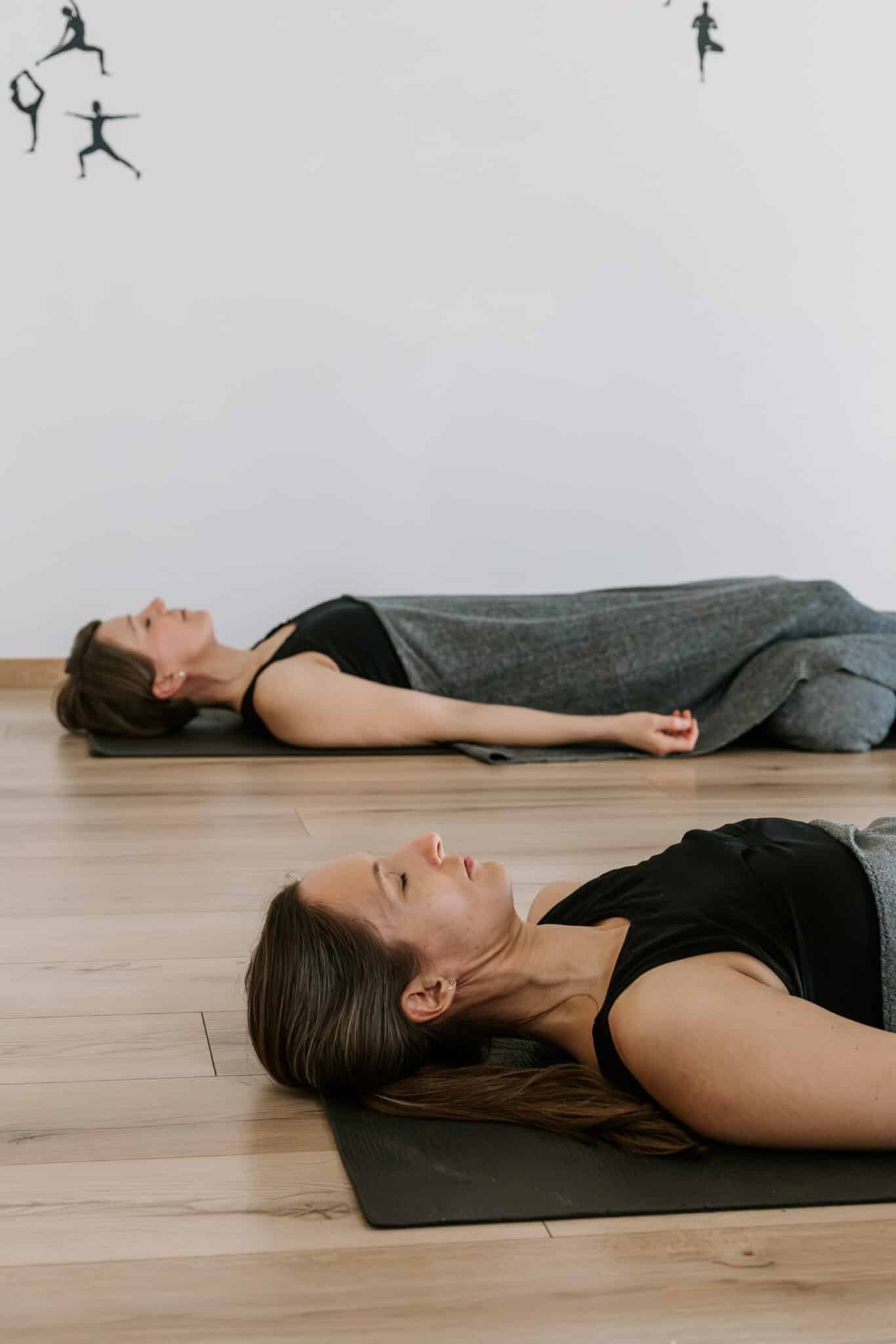 To kvinder ligger på ryggen på yogamåtter i dyb afspænding under en session med MediYoga